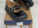 des chaussures d'école noires ornées de boucles dorées, posées sur une boîte en carton