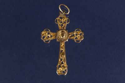 une croix en or sur laquelle est représenté un oiseau est suspendue à une chaîne