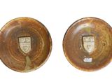 two brown pottery plates with a crest on them on a white surface