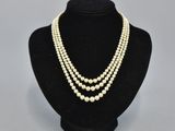a white pearl necklace with three strands of pearls on a black mannequin