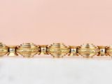 an image of a gold plated bracelet on a pink background
