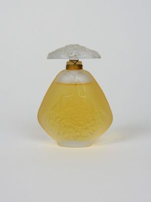 flacon de parfum en verre jaune avec un bouchon blanc, posé sur une surface blanche
