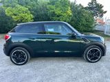une Mini Cooper verte garée sur un parking, près des buissons