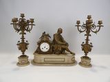 une statue représentant un homme assis sur une table, à côté de trois chandeliers