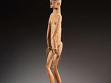une statue en bois représentant un homme debout sur un socle noir
