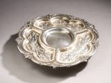 an antique silver plate on a table with a shadow on the ground