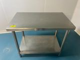 une table en acier inoxydable avec une étagère en dessous, posée sur un sol bleu