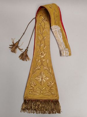 un ancien collier brodé de doré et de rouge, orné de pompons suspendus sur le côté