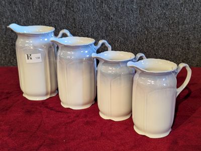 quatre pichets blancs sont alignés sur une nappe rouge