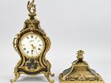 une horloge ancienne et une petite horloge posées sur une surface blanche