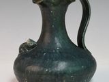 un vase vert muni d'une anse, posé sur une surface blanche