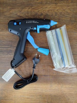 un pistolet à colle, des bâtons de colle et un sac en plastique posés sur une table