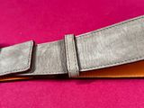 a close up of a wallet with a leather strap on a pink surface