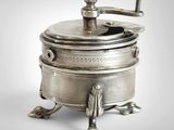 un moulin à café ancien en métal argenté, posé sur un socle