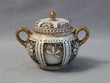 a white and gold vase with a lid on a table