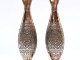 two silver vases sitting next to each other on a white surface