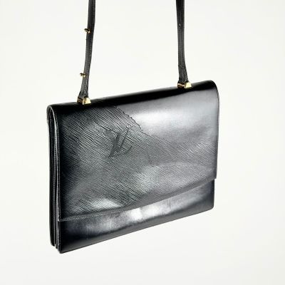 sac à main en cuir noir avec des finitions dorées et une bandoulière, sur fond blanc
