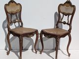 pair of antique wooden chairs with cane seats against a white wall