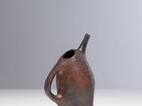 un petit vase brun posé sur une surface blanche