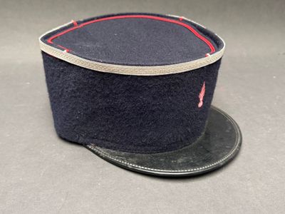 un bonnet bleu marine avec une bordure rouge sur le dessus, posé sur une surface grise