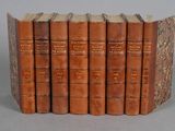 six old books are lined up in a row on a gray surface