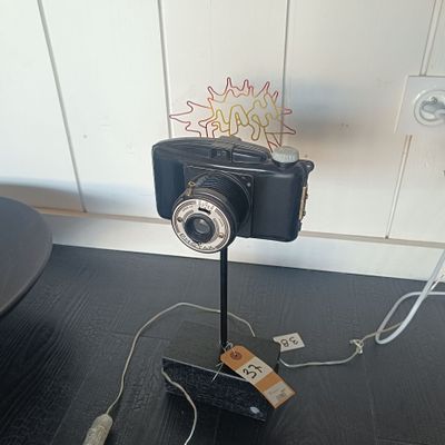 une image représentant un appareil photo posé sur un trépied, avec une étiquette de prix accrochée dessus