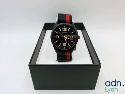 une montre noire et rouge dans un coffret noir posé sur une surface blanche
