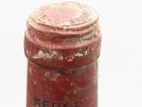 a red bottle with a black label sitting on a white surface