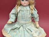 an antique doll sitting on a red surface wearing a dress and hat