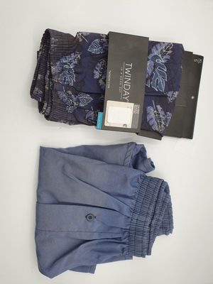 deux paires de pantalons de costume pour homme et une cravate posés sur une surface blanche