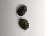 two green tourmaline gems sitting on top of a white surface