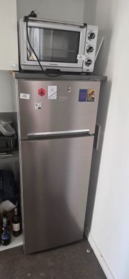 un réfrigérateur argenté dans une petite cuisine, avec un micro-ondes posé dessus