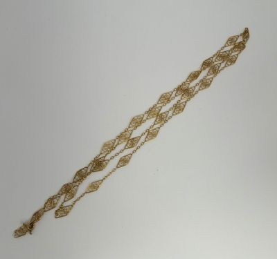 a close up of a gold bracelet with a chain on a white surface