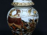 a white and gold vase with a lid on a black background