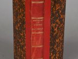 an old book with a red cover sitting on top of a table