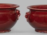 une paire de vases rouges munis d'anses, posés sur une surface grise