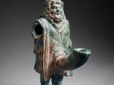 an ancient bronze figurine of a man holding a fish