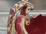 a red vase with a bird on it sitting on a window sill