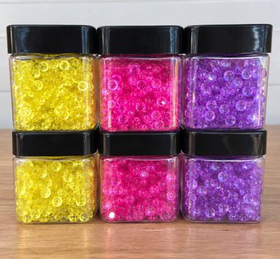 quatre bocaux remplis de perles de différentes couleurs posés sur une table en bois
