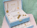 a small blue box with jewelry in it on a pink table