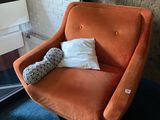 an orange chair with a pillow on it in front of a window