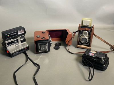 trois appareils photo et un étui à appareil photo posés sur une table, avec une sangle d'appareil photo