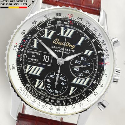 the black dial of a watch with roman numerals on a brown leather strap