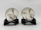 pair of porcelain cups and saucers with floral designs on them