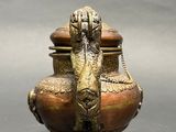 a bronze vase with a bird on it on a table