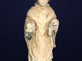une vieille statue représentant un homme coiffé d'un chapeau et vêtu d'une robe