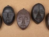 Quatre masques africains sculptés sont alignés sur une surface marron