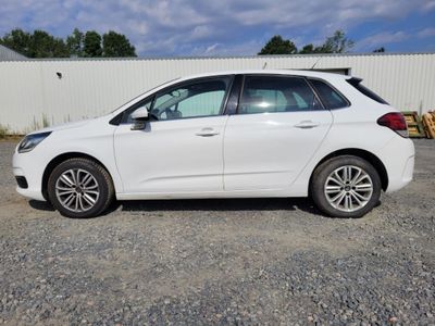 La voiture blanche est garée sur le parking, à côté d'une clôture.