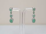a pair of emerald and diamond earrings on a stand