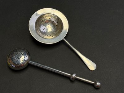 two spoons and a strainer on a black surface